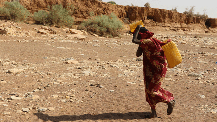 woman carrying water container on dry land in ethiopia hunger