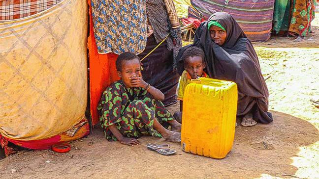 two children and a mother sat outside their home with a yellow water container
