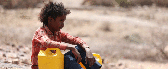 child in yemen sat on dry land next to a yellow water container hunger