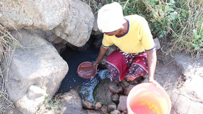 a young woman in malawi drawing water from a shallow water well