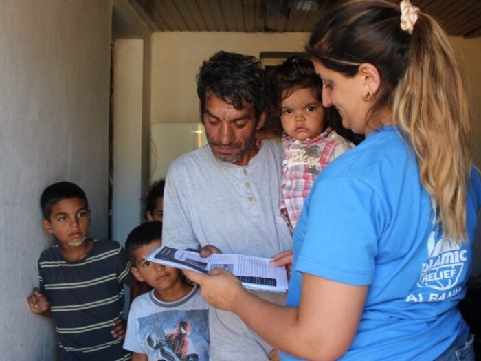 a man from albania named julian is holding his child and receiving a pack of qurbani meat from islamic relief