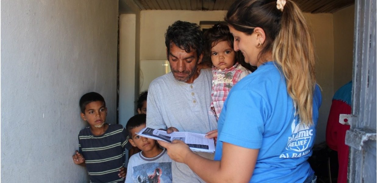 a man from albania named julian is holding his child and receiving a pack of qurbani meat from islamic relief