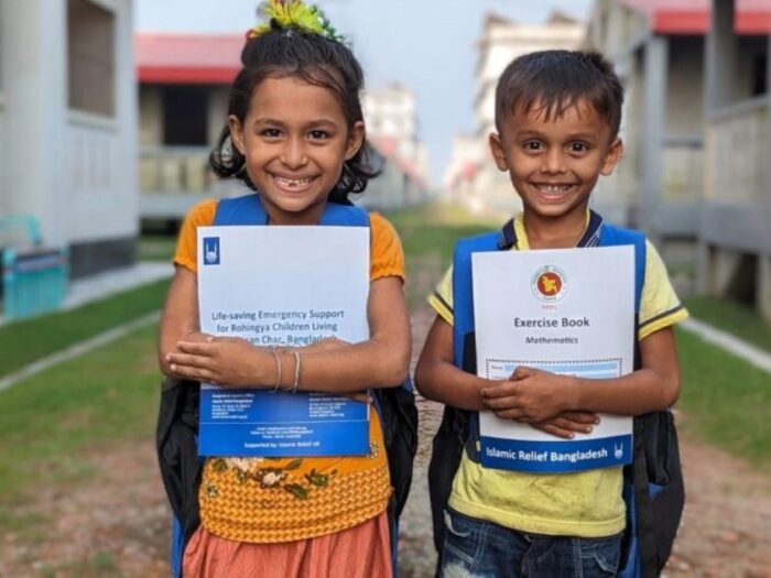 two children who are rohingya refugees residing in camps in bangladesh are smiling to camera as they hug new textbooks they have received from islamic relief