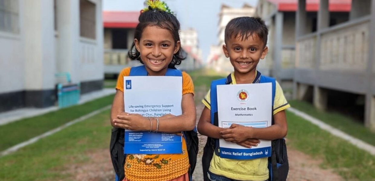 two children who are rohingya refugees residing in camps in bangladesh are smiling to camera as they hug new textbooks they have received from islamic relief