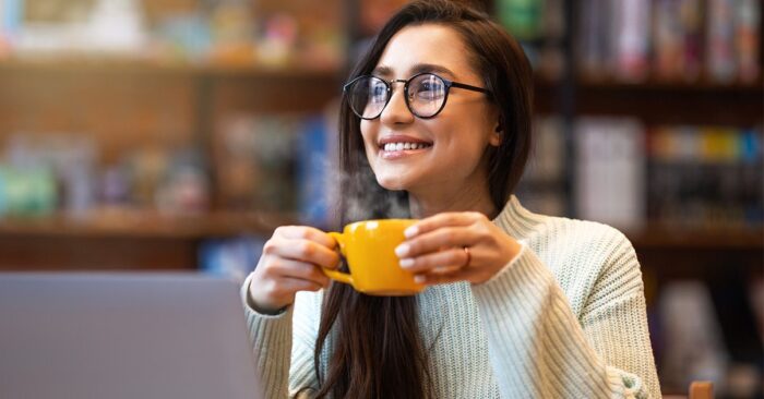 A lady drinking a cup of coffee and smiling.