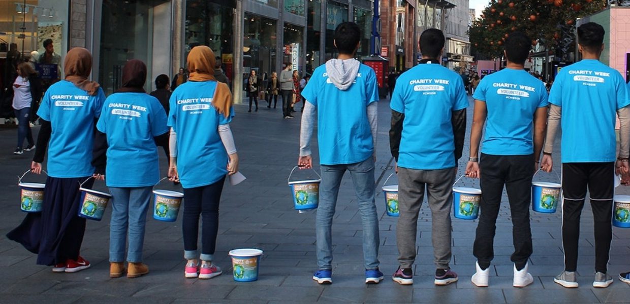 a group of people in charity week t-shirts holding buckets on a sidewalk islamic relief