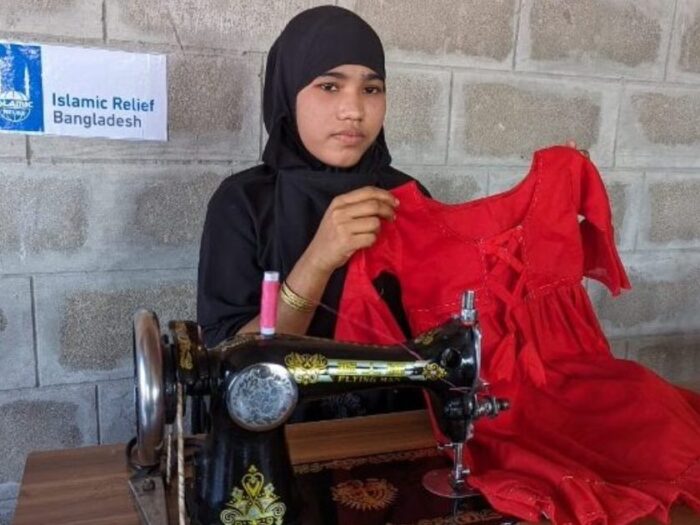 a young teenage girl from bangladesh holding a red dress she sew