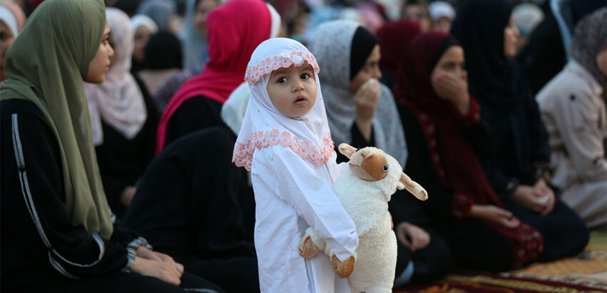 little girl in prayer clothes holding a toy sheep at eid prayer for eid ul adha in palestine