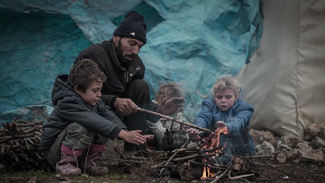 a father and his three children in syria keeping themselves warm around an open fire