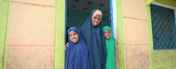 a woman and her two children at a doorway, orphan family sponsorship by islamic relief