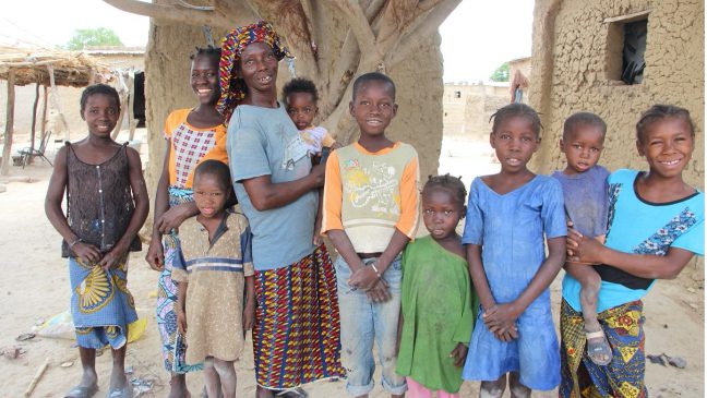 a malian woman called Fatoumata wearing a grey t-shirt and a colourful head wrap, standing with her family and children