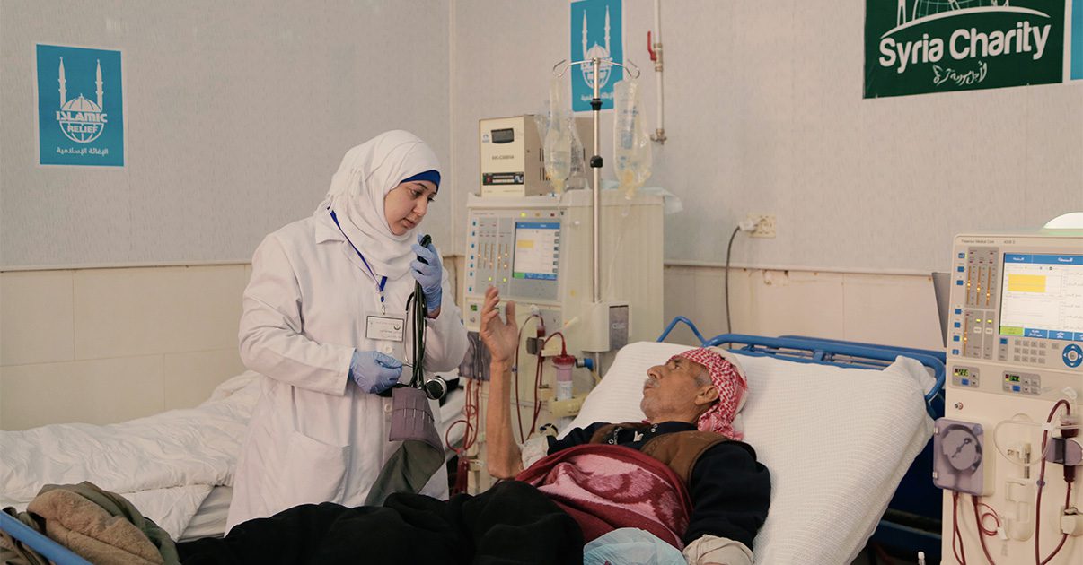 A patient lies in a hospital bed receiving dialysis and speaks to doctor.