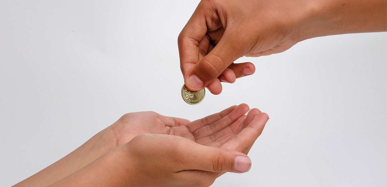 one hand giving a coin to another hand sadaqah on behalf of someone