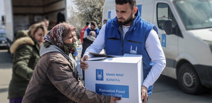 Ramadan Islamic Relief staff member handing lady a food parcel.