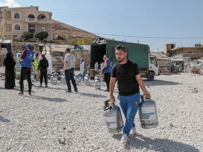 a person carrying two fire extinguishers to distribute to syrian refugees in a camp in lebanon