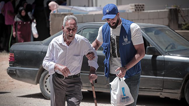 islamic relief staff in jordan helping a man walk while holding a bag of qurbani meat local teams