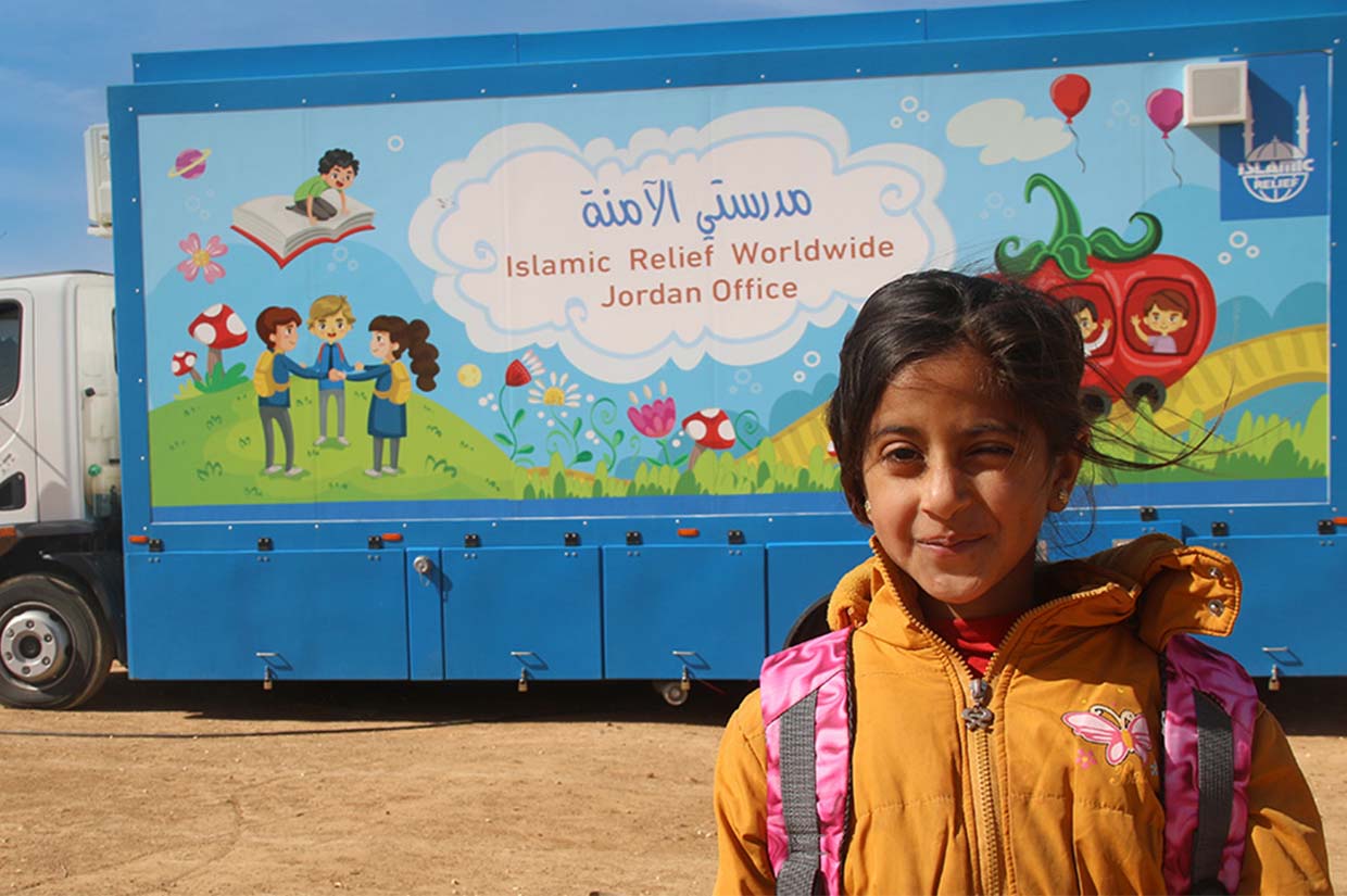 young girl standing in front of a mobile classroom in jordan provided by islamic relief