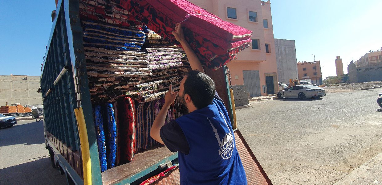 man in blue islamic relief jacket loading a truck with mattress to be distributed to victims of the morocco earthquake