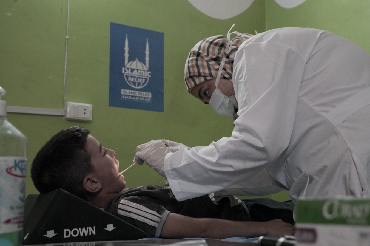 a female nurse looking into the mouth of a young child orphan medical care islamic relief