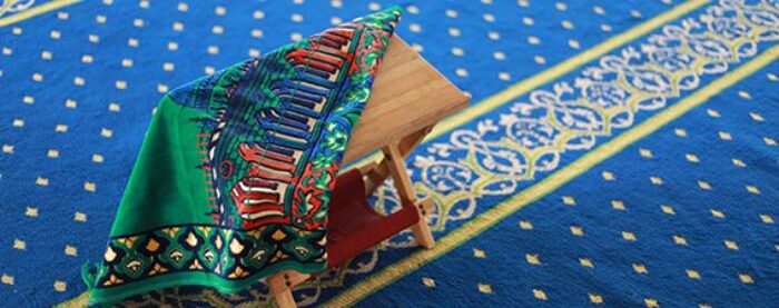 prayer mat on quran stand on a blue masjid carpet prayer timetables