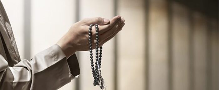 man with hands open infront of him for dua with prayer beads (tasbih) in his hand prayer timetables