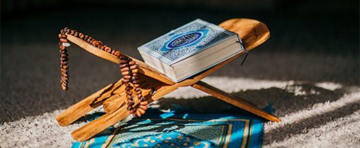 quran and prayer beads (tasbih) on quran stand on blue prayer (salah) mat prayer timetables