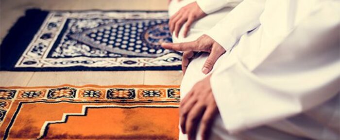 Two men on prayer mats raising one finger during prayer salah prayer timetables