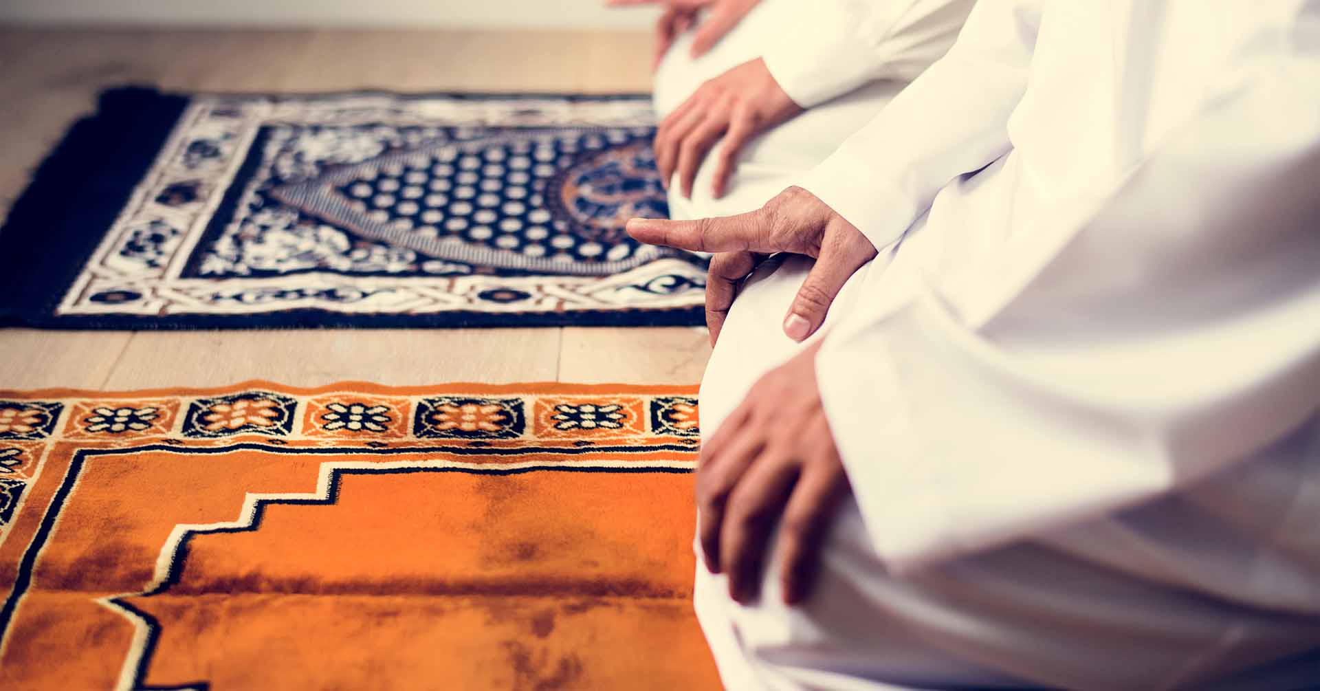 Two men on prayer mats raising one finger during prayer salah prayer timetables slough