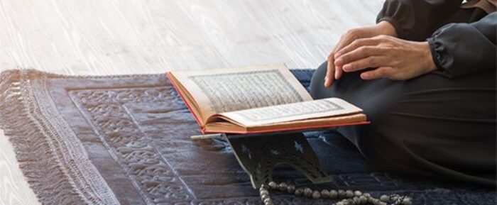 man with an open quran in front of him on a blue prayer salah mat prayer timetables