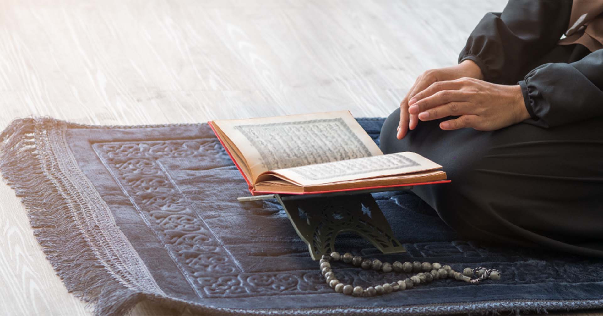 man with an open quran in front of him on a blue prayer salah mat prayer timetables birmingham