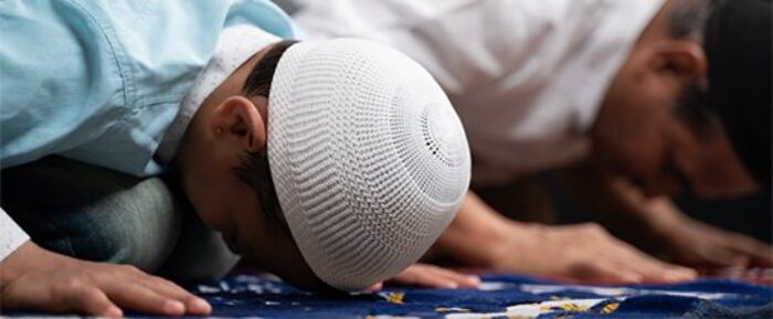 elderly man and young boy on prayer mats in sujood position prayer timetables