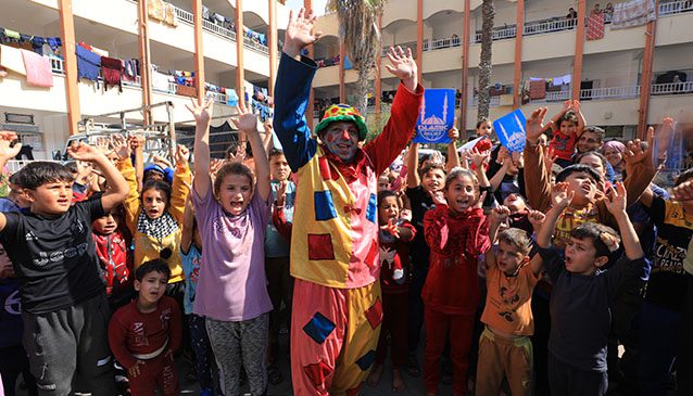 a man dressed as a clown playing with children in a courtyard in gaza