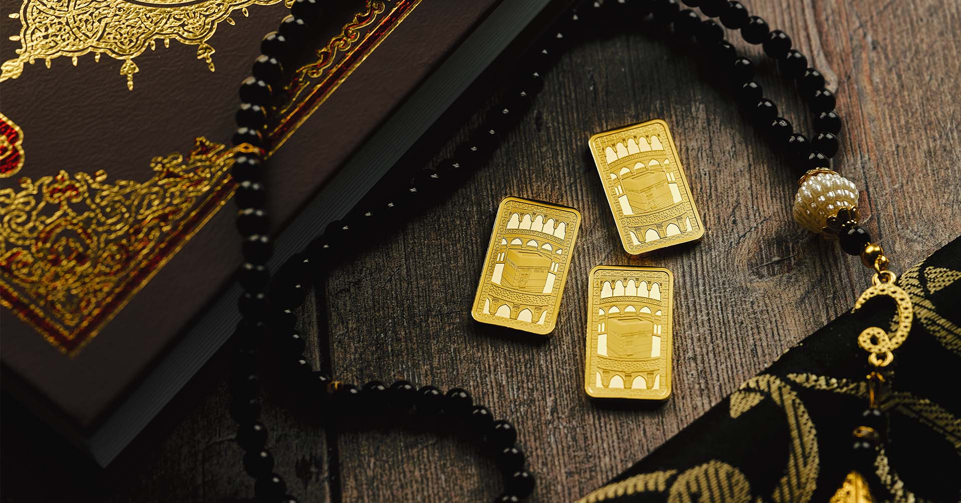 three gold bars with a kaaba design by the royal print on a table next to a black and gold quran and black tasbih prayer beads islamic relief uk partnership