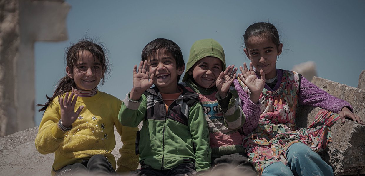Children in Syria smiling and waving at the camera sadaqah
