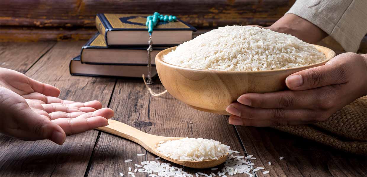 bowl of rice in one persons hands being given to another person's hands that is empty with quran and prayer beads (tasbih) in the background zakat sadaqah