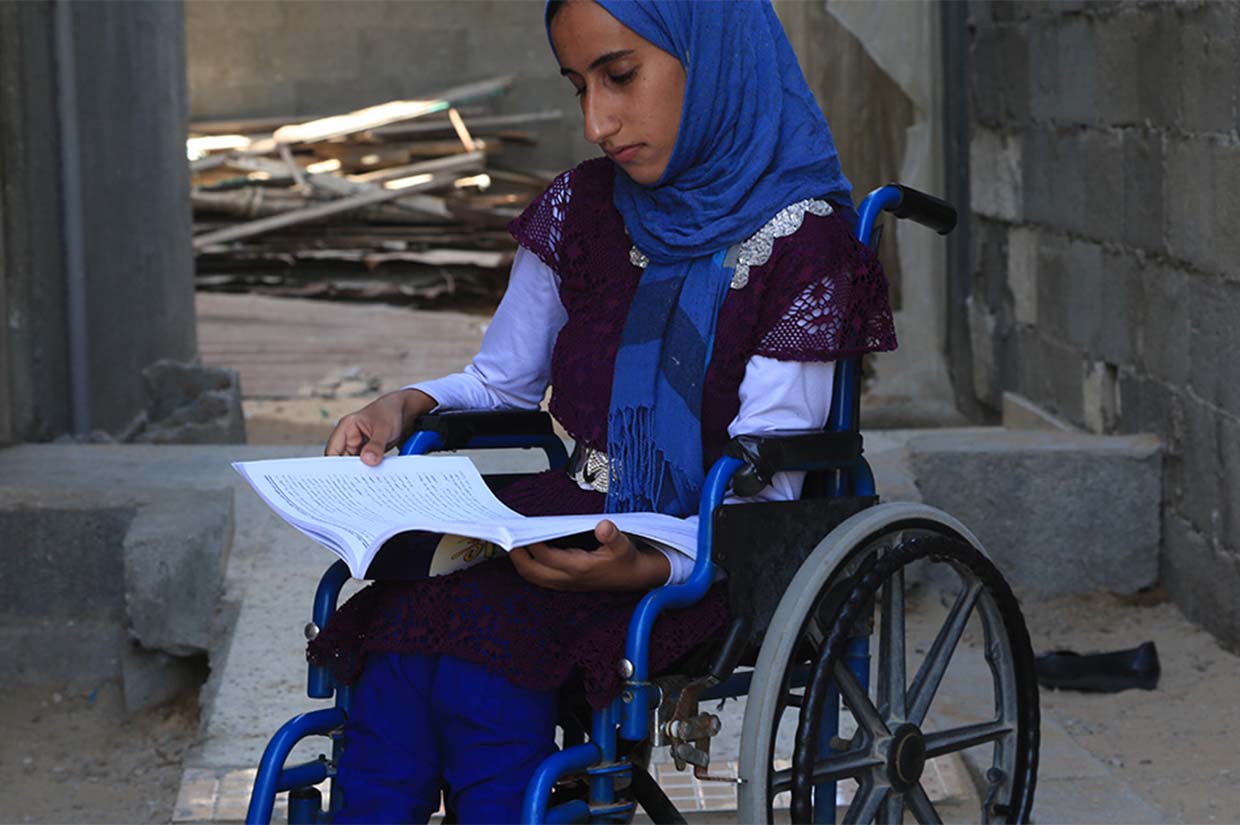 young girl sat in a wheelchair writing in a textbook