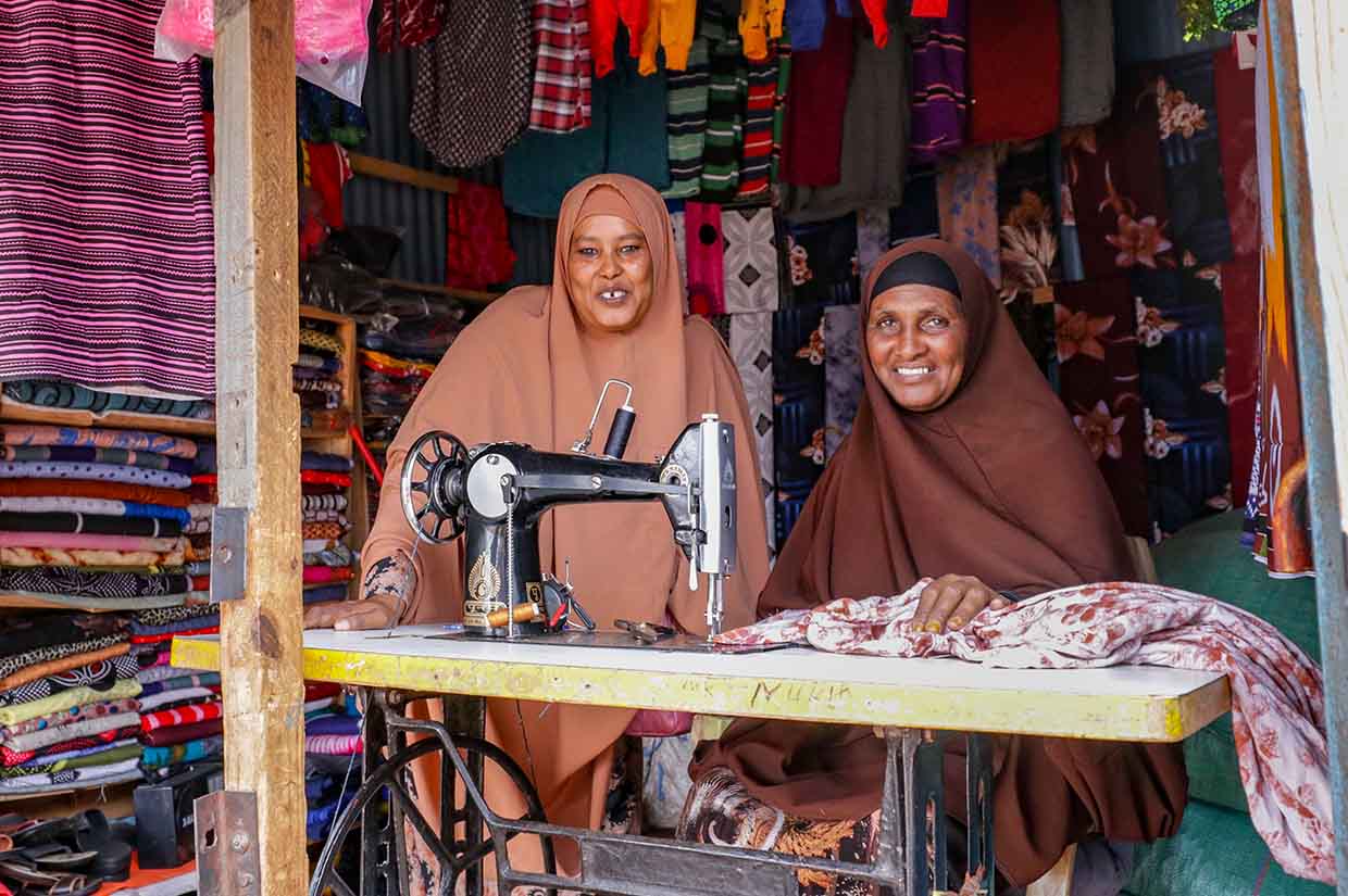 two women smiling next to a sewing machine