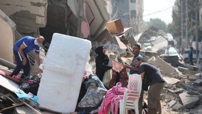 a group of people in gaza standing next to debris from destroyed buildings following recent airstrikes