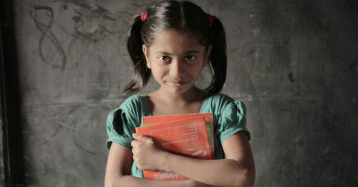 young girl with black hair in two ponytails holding a red book