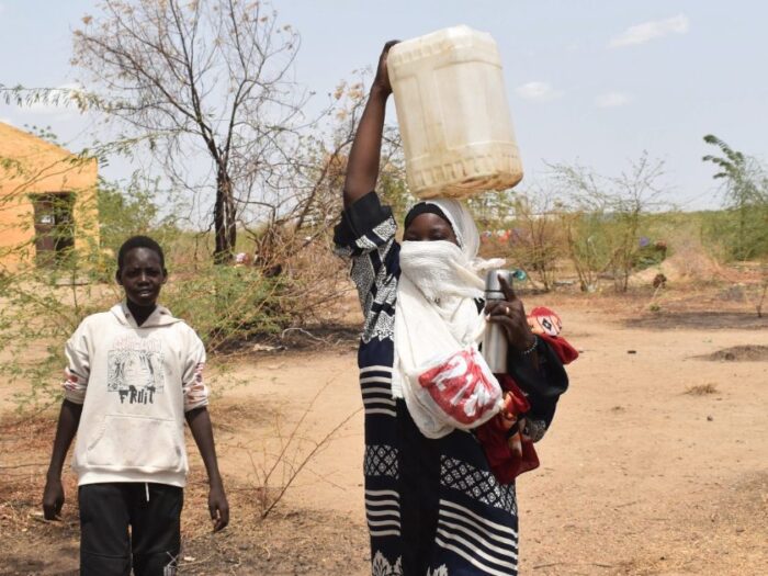 a sudanese woman carrying a water container over her head