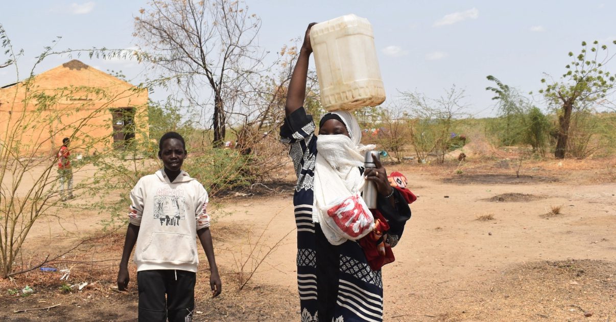 a sudanese woman carrying a water container over her head