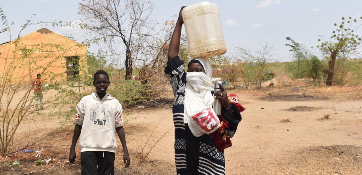 a sudanese woman carrying a water container over her head