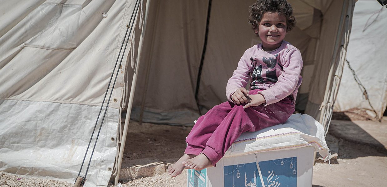 Young girl sat on Islamic Relief's Ramadan food box