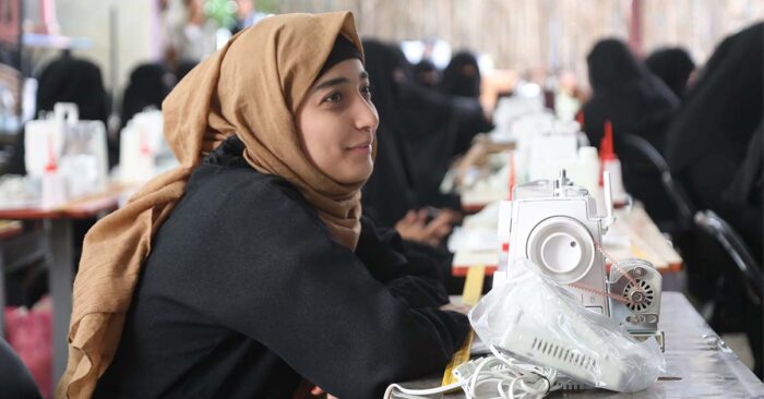 a girl in hijab leaning over the table with a sewing machine in front of her vocational training