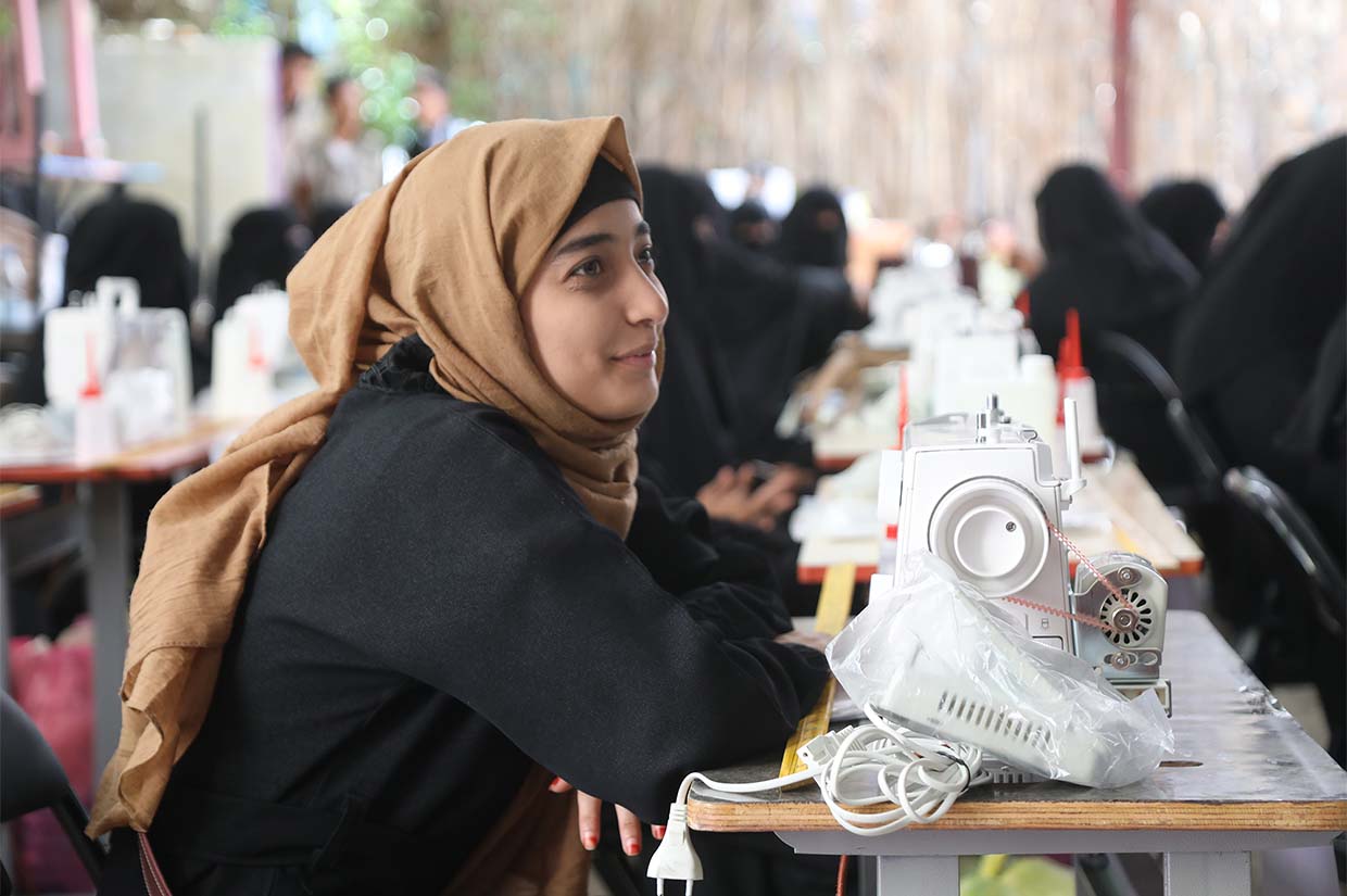 a girl in hijab leaning over the table with a sewing machine in front of her vocational training