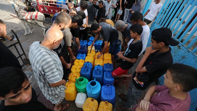 a group of men in gaza standing around a water tap with water containers