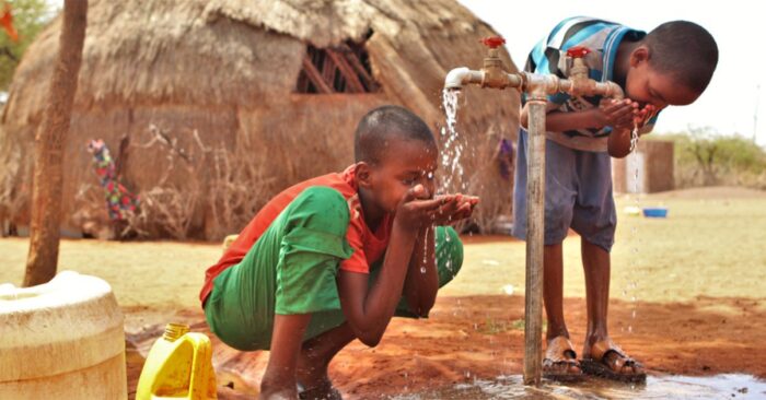 two boys drinking clean water from a water pump