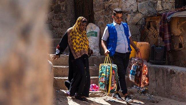 an islamic relief staff member supporting a yemeni woman with her winter supplies provided by islamic relief