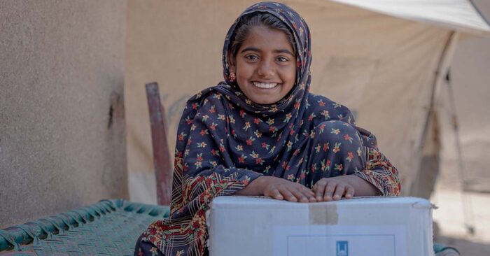 young girl in pakistan smiling with a zakat ul fitr donation box of food from islamic relief uk