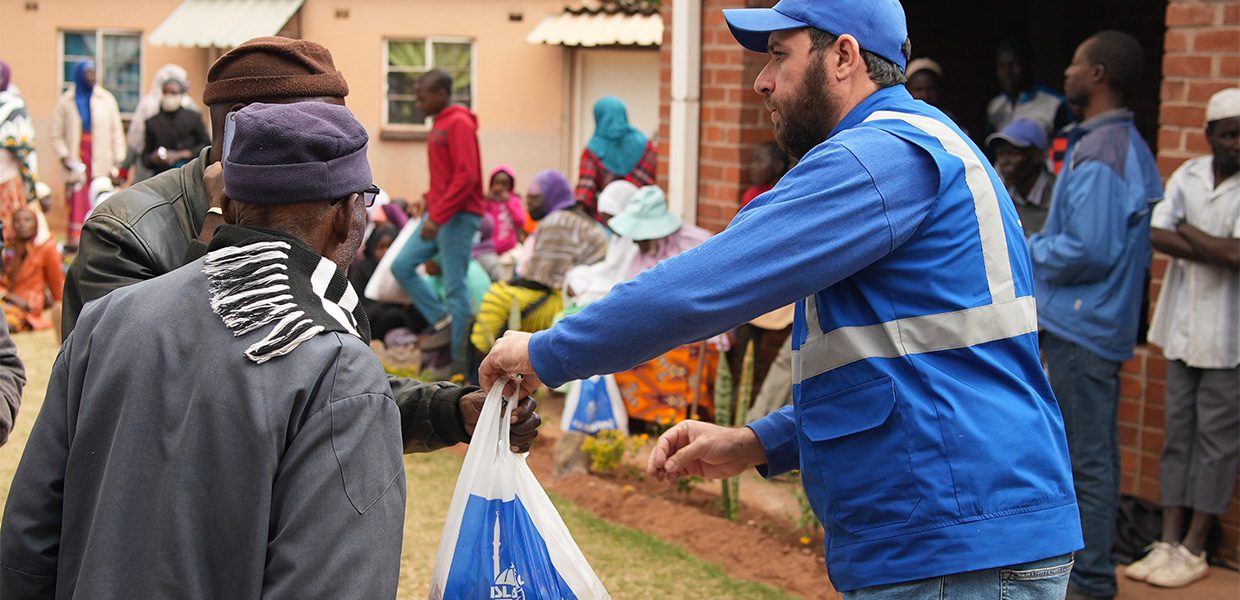 An Islamic Relief staf member hands a bag of qurbani meat to a beneficiary